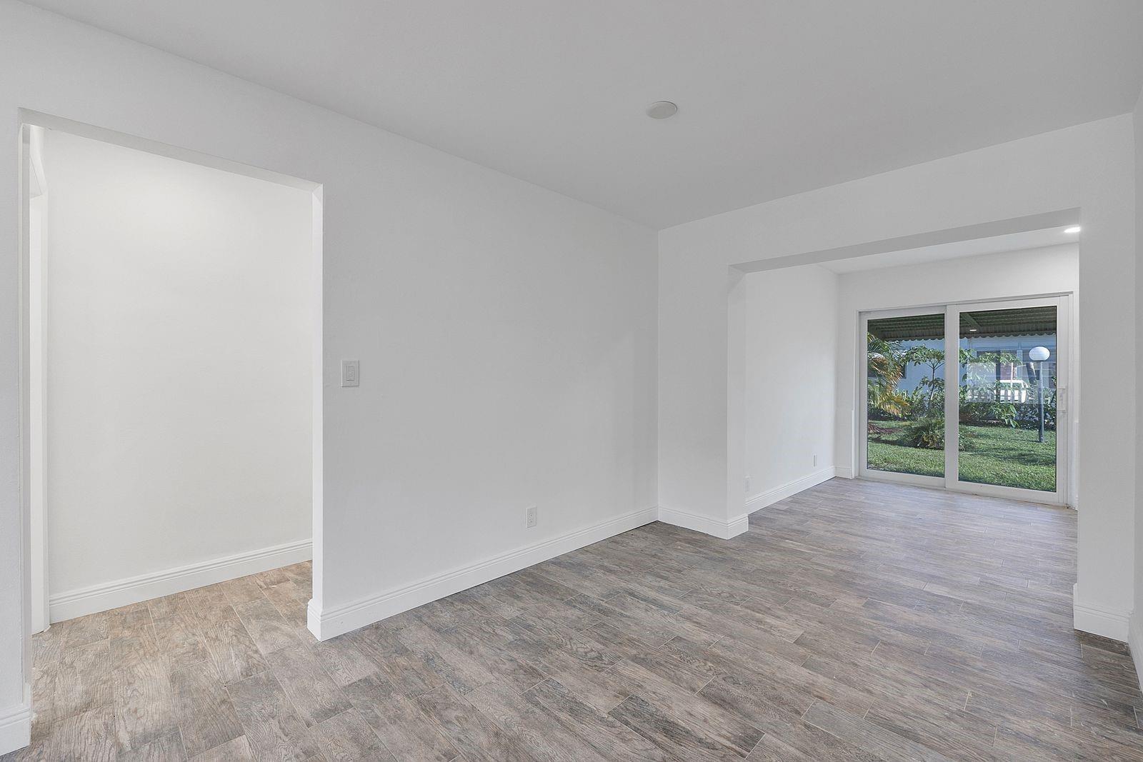 An empty room with white walls, wood-look tile flooring, and a sliding glass door — 370 S Golf Boulevard, Pompano Beach FL 33064, POMPANO BEACH, FL