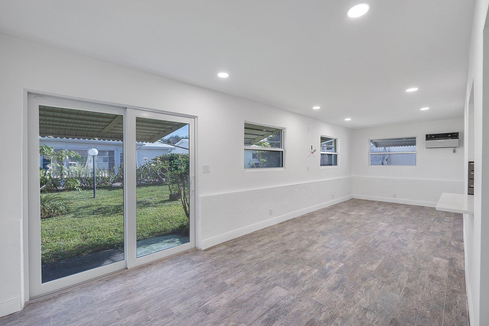 A bright, empty room features white walls, wood-look tile flooring, recessed lighting, and sliding glass doors — 370 S Golf Boulevard, Pompano Beach FL 33064, POMPANO BEACH, FL
