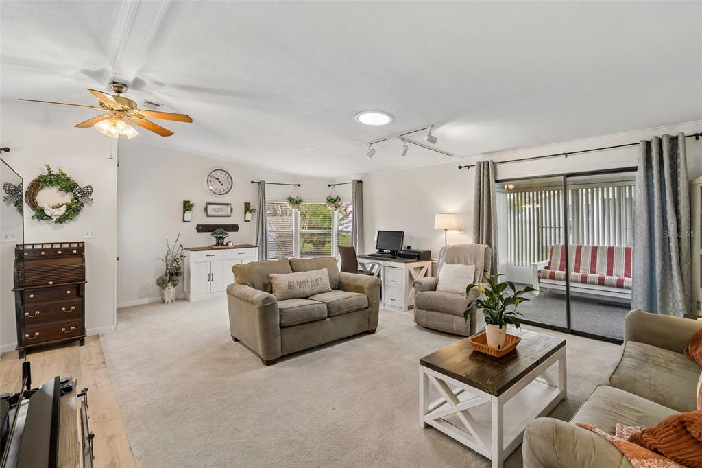 A living room features beige carpet, a ceiling fan, a desk, and sliding glass doors — 25201 CLIFFORD, LEESBURG, FL
