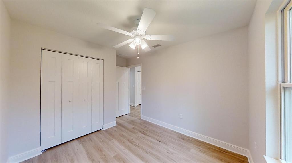 A bedroom with light wood-look flooring, a white ceiling fan, and a white bi-fold closet — 24304 NW TAMARIND LANE, DUNNELLON, FL
