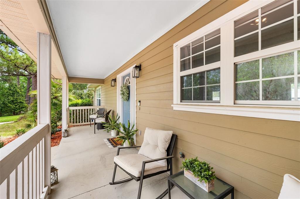 A covered front porch features tan siding, a blue door, and outdoor seating furniture — 14659 NW 150TH PLACE, ALACHUA, FL