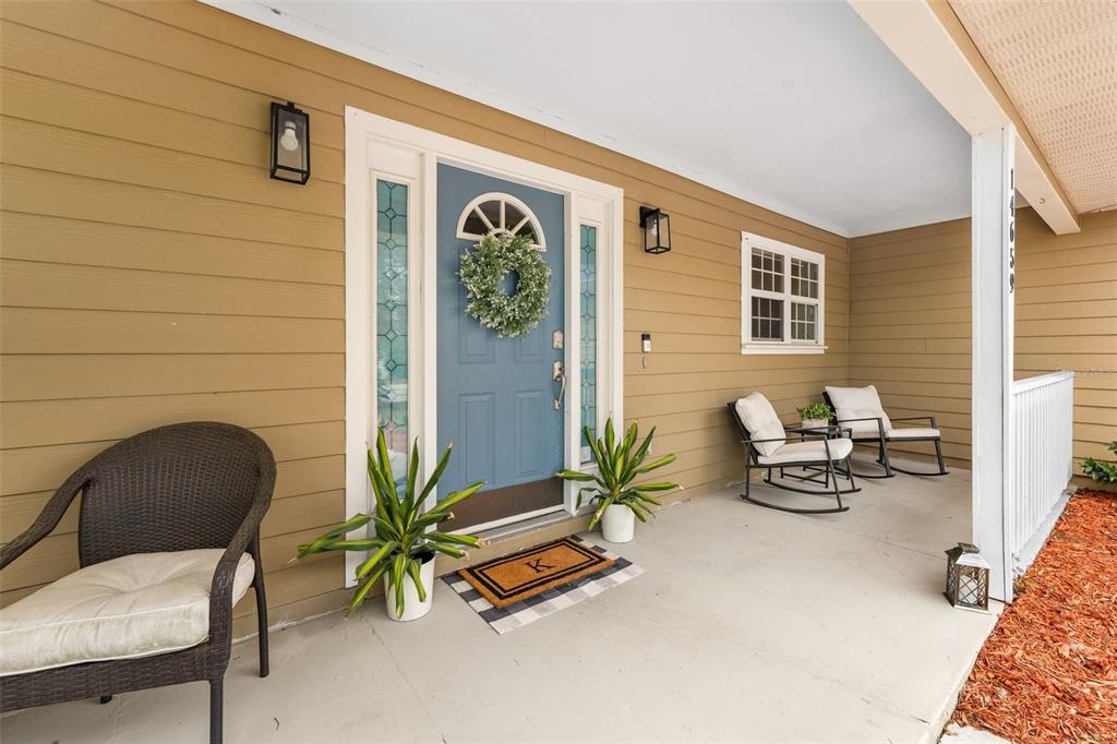 A covered front porch features a blue door, two rocking chairs, and a wicker chair — 14659 NW 150TH PLACE, ALACHUA, FL
