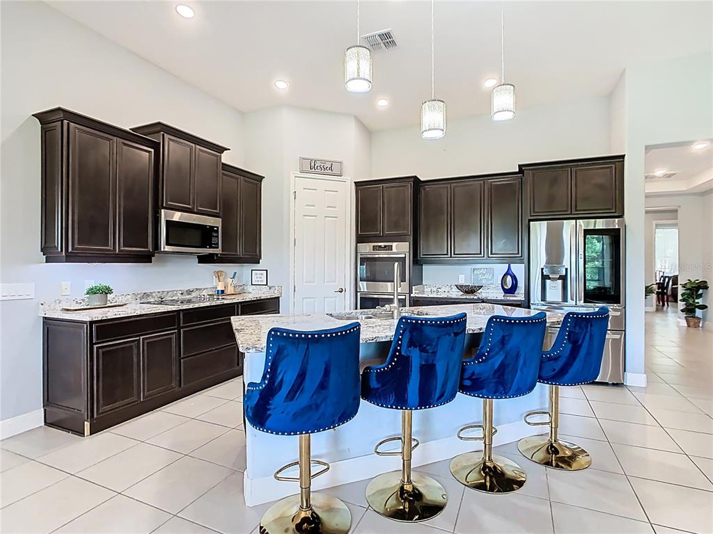 A kitchen features dark wood cabinets, granite countertops, a center island, and blue bar stools — 3231 AGOSTINO TER, KISSIMMEE, FL