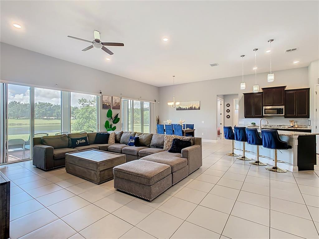 An open-concept living room and kitchen featuring a large sectional sofa and breakfast bar seating — 3231 AGOSTINO TER, KISSIMMEE, FL