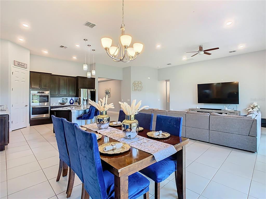 A dining area with blue chairs and a wooden table sits before an open-concept kitchen — 3231 AGOSTINO TER, KISSIMMEE, FL