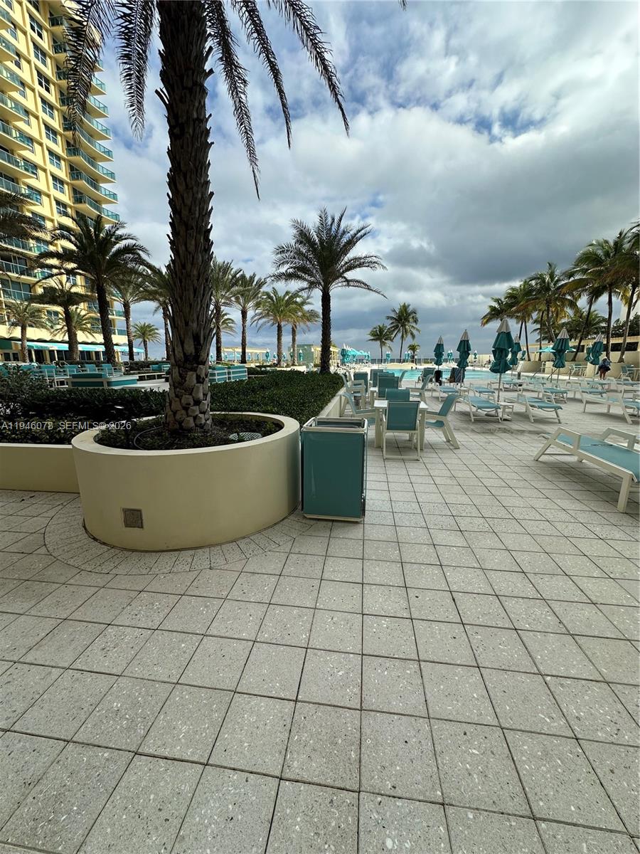A paved pool deck features lounge chairs, tables, palm trees, and a tall building — 2501 S Ocean Dr # 507, Hollywood FL 33019, HOLLYWOOD, FL
