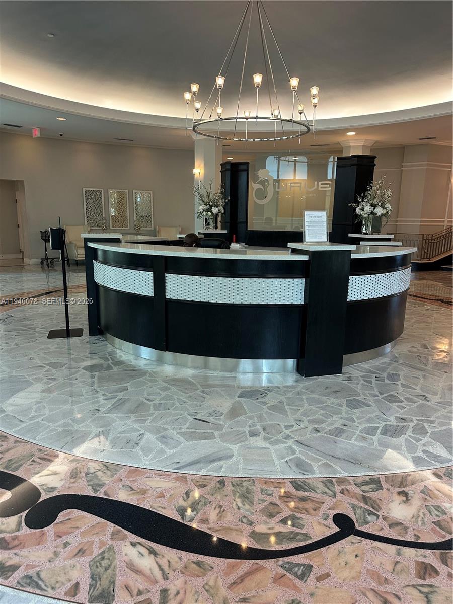 A curved reception desk sits in a lobby with a chandelier and marble flooring — 2501 S Ocean Dr # 507, Hollywood FL 33019, HOLLYWOOD, FL