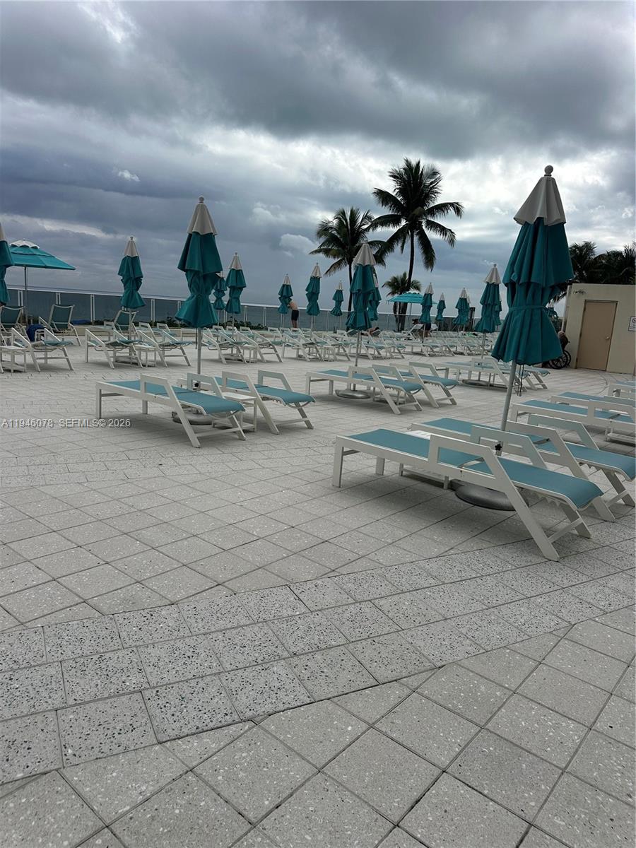 A pool deck features numerous lounge chairs and teal umbrellas under a cloudy sky — 2501 S Ocean Dr # 507, Hollywood FL 33019, HOLLYWOOD, FL
