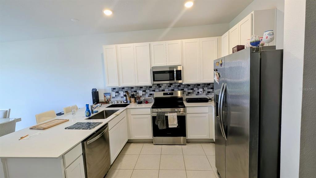 A kitchen features white cabinets, stainless steel appliances, a tiled backsplash, and a large island — 3010 CHANTILLY DRIVE, DAVENPORT, FL