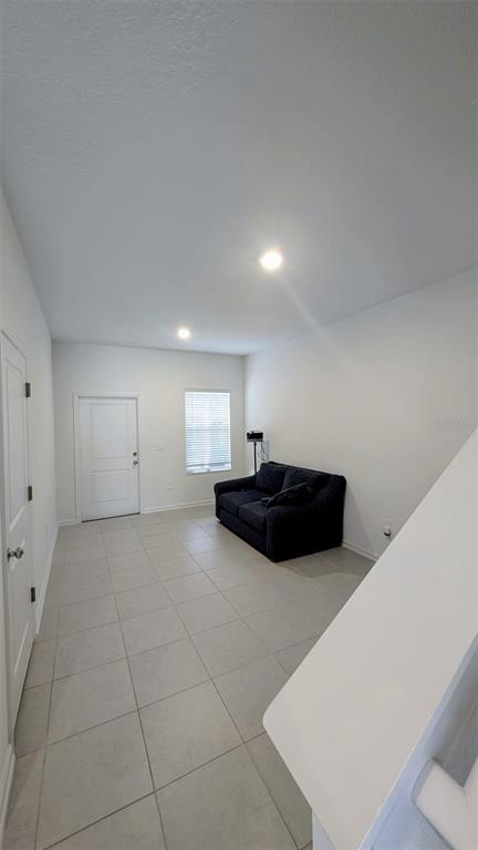A living room with light tile flooring, white walls, a dark sofa, and a door — 3010 CHANTILLY DRIVE, DAVENPORT, FL