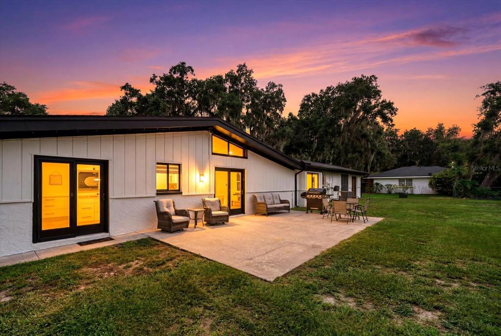 A backyard patio with outdoor furniture sits behind a white house at sunset — 3518 BERGER ROAD, LUTZ, FL
