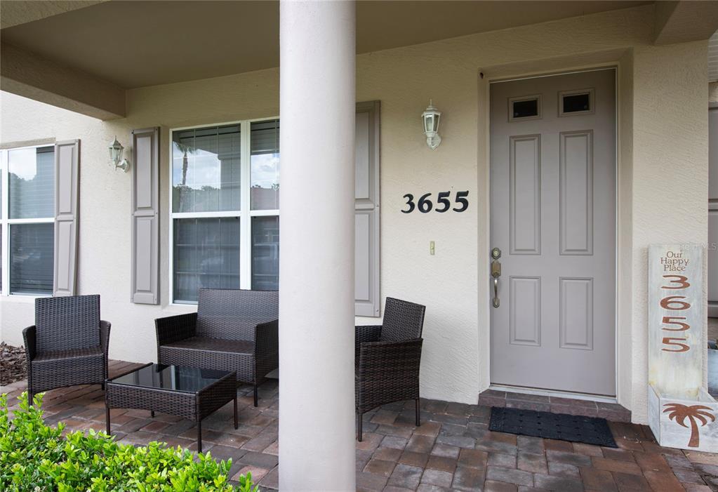 A covered front porch features a paved floor, wicker furniture, and a light-colored door — 3655 CASALTA CIRCLE, NEW SMYRNA BEACH, FL