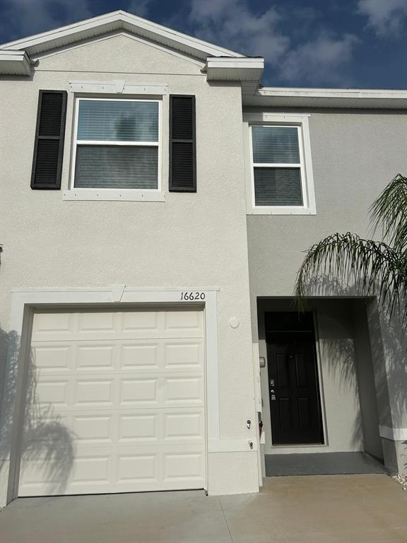 A two-story townhouse exterior features a white garage door, a black front door, and shutters — 16620 GROTTO STEAM PLACE, WIMAUMA, FL