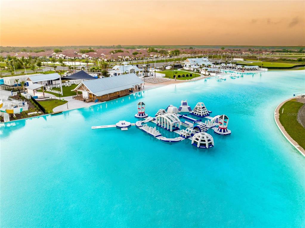 An aerial view shows a large turquoise lagoon with an inflatable obstacle course — 16620 GROTTO STEAM PLACE, WIMAUMA, FL