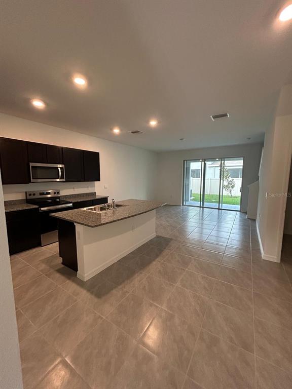 A kitchen with dark cabinets and a granite island opens into a tiled living area — 16620 GROTTO STEAM PLACE, WIMAUMA, FL
