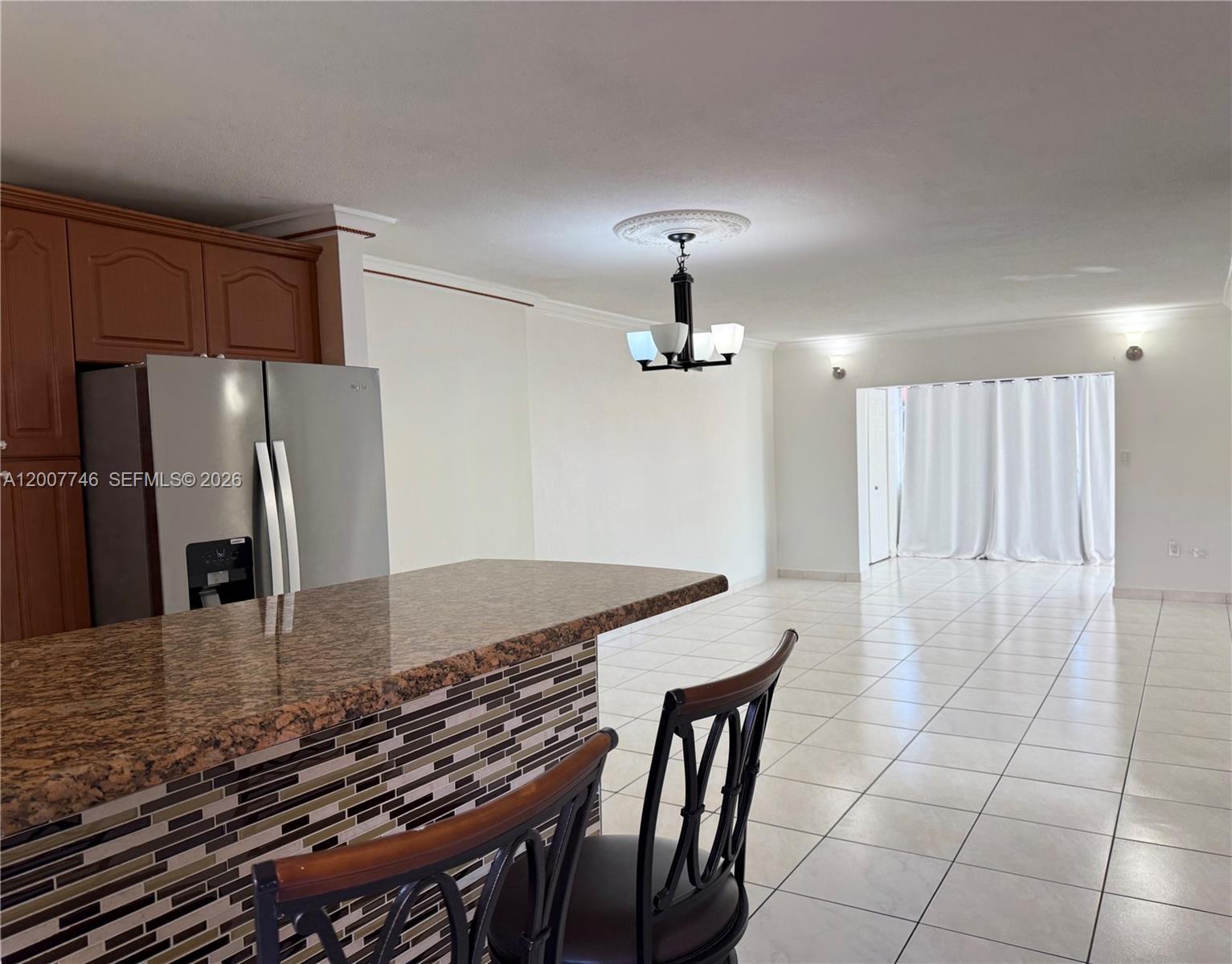 A kitchen with a granite breakfast bar and stainless steel refrigerator overlooks a tiled living area — 1850 W 56th St # 2404, Hialeah FL 33012, HIALEAH, FL