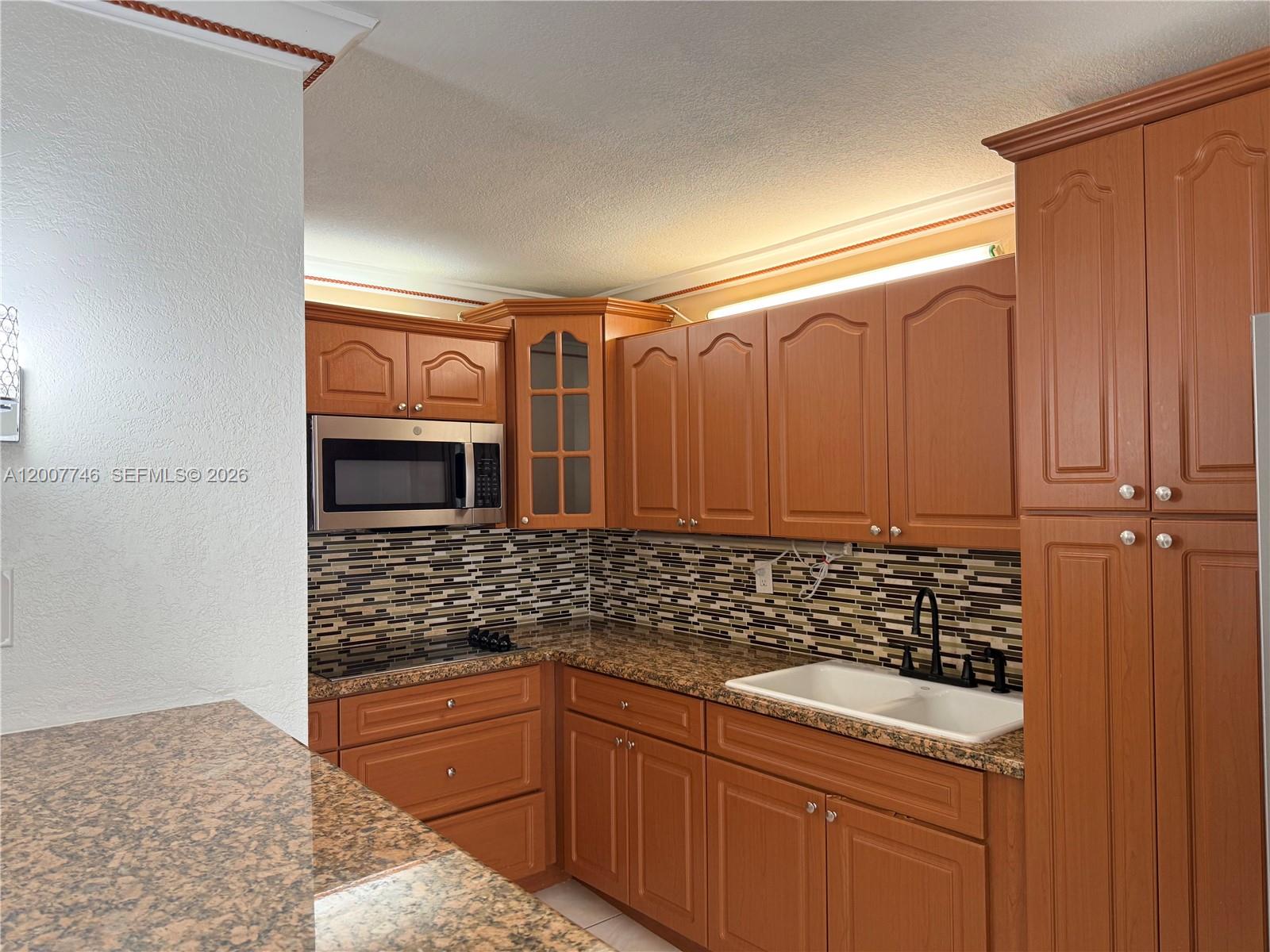 A kitchen features wood cabinets, granite countertops, a mosaic backsplash, and stainless steel appliances — 1850 W 56th St # 2404, Hialeah FL 33012, HIALEAH, FL
