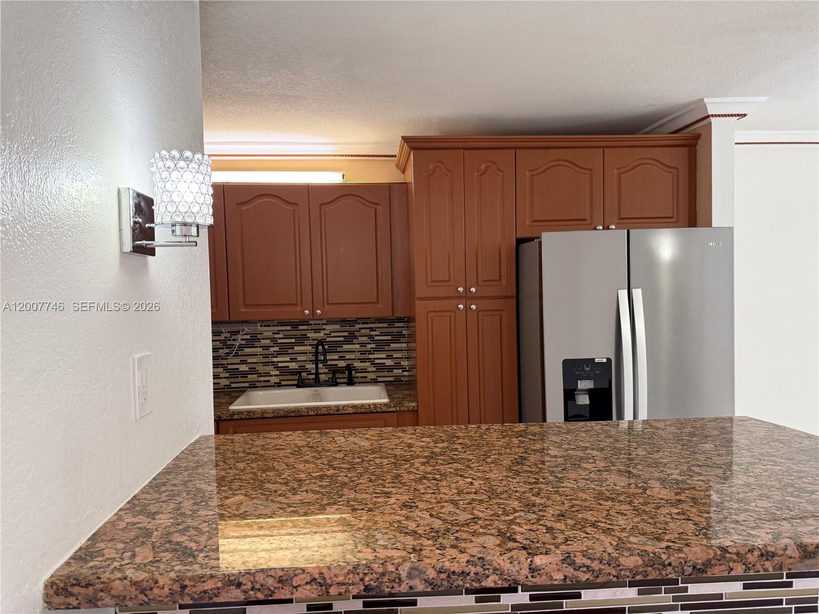 A kitchen features brown wood cabinets, granite countertops, a stainless steel refrigerator, and mosaic backsplash — 1850 W 56th St # 2404, Hialeah FL 33012, HIALEAH, FL