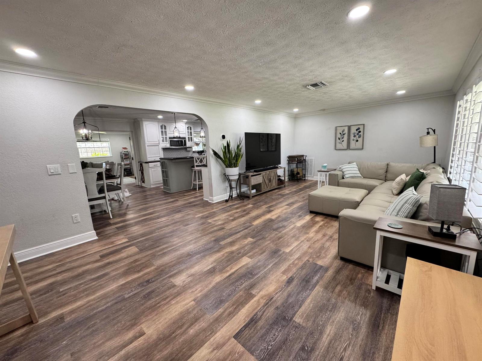 A spacious living room with wood-look flooring opens into a kitchen with white cabinetry — 7828 Saint Andrews Road, Lake Worth FL 33467, LAKE WORTH, FL