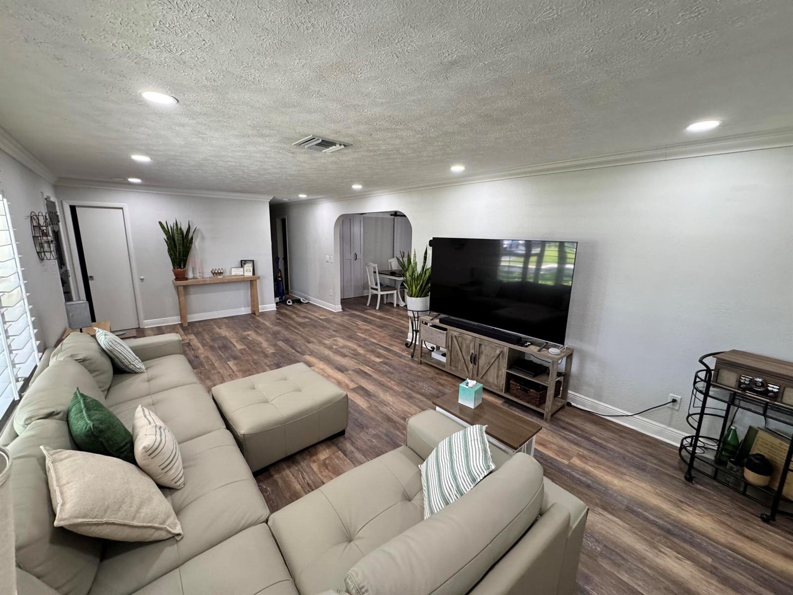 A living room features a sectional sofa, a large television on a console, and wood-look flooring — 7828 Saint Andrews Road, Lake Worth FL 33467, LAKE WORTH, FL