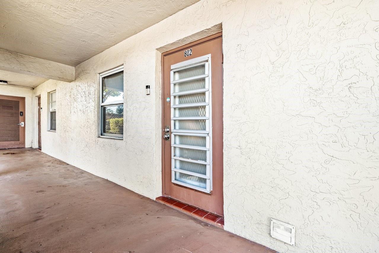 An exterior view of a building hallway featuring a brown door numbered 802 — 9280 SW 3rd Street # 802, Boca Raton FL 33428, BOCA RATON, FL