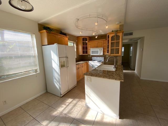 A kitchen features light wood cabinets, granite countertops, a white refrigerator, and tile flooring — 183 Andover H, West Palm Beach FL 33417, WEST PALM BEACH, FL