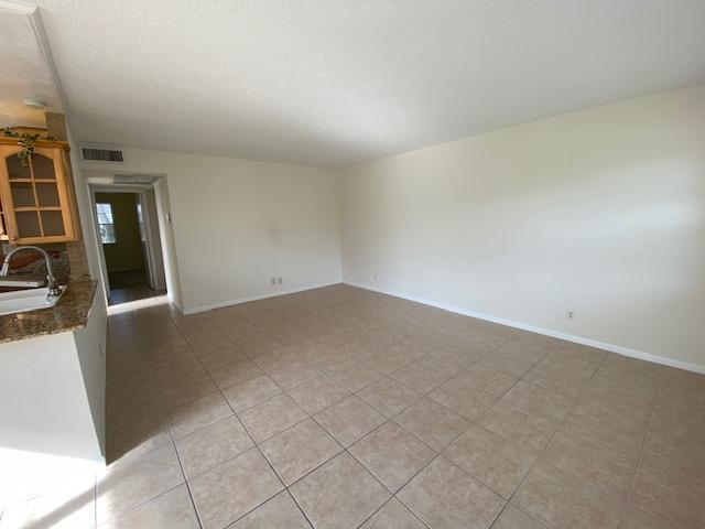 A spacious room with light-colored tile flooring and plain walls, adjacent to a kitchen area — 183 Andover H, West Palm Beach FL 33417, WEST PALM BEACH, FL