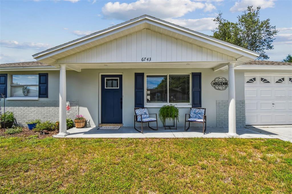 A single-story house exterior features a covered porch, blue front door, and a garage — 6743 KNIGHTSBRIDGE DRIVE, NEW PORT RICHEY, FL