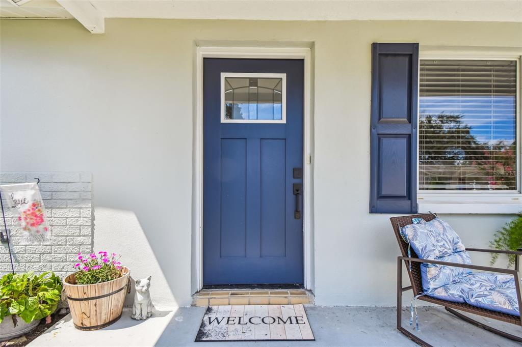 A blue front door with a window sits on a porch with a welcome mat — 6743 KNIGHTSBRIDGE DRIVE, NEW PORT RICHEY, FL
