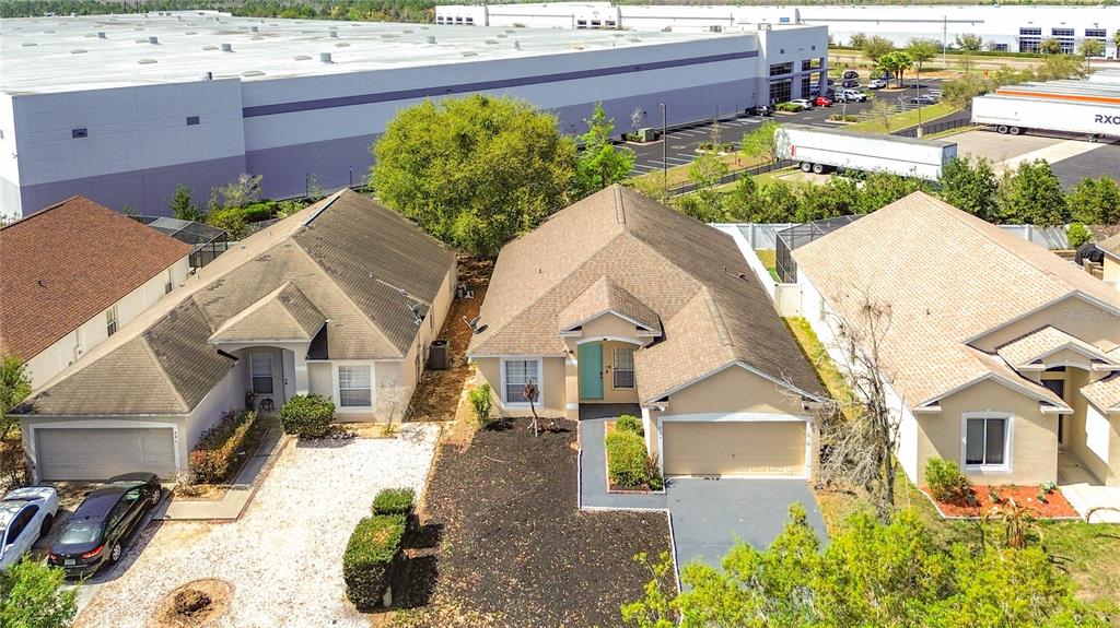 An aerial view shows three suburban houses situated in front of a large industrial warehouse — 635 KNOLLWOOD DRIVE, DAVENPORT, FL