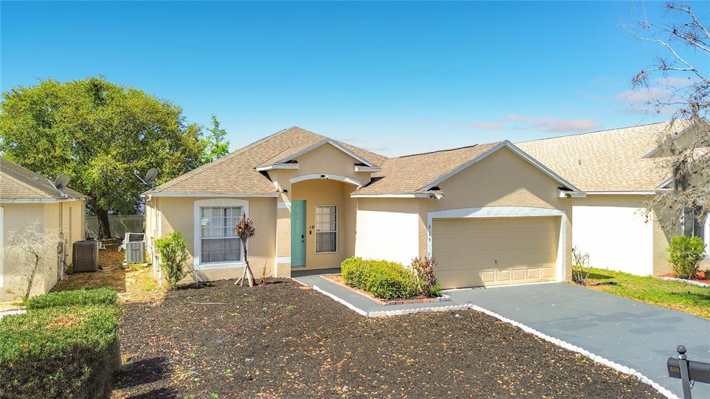A single-story house with a tan stucco exterior, a two-car garage, and a front yard — 635 KNOLLWOOD DRIVE, DAVENPORT, FL