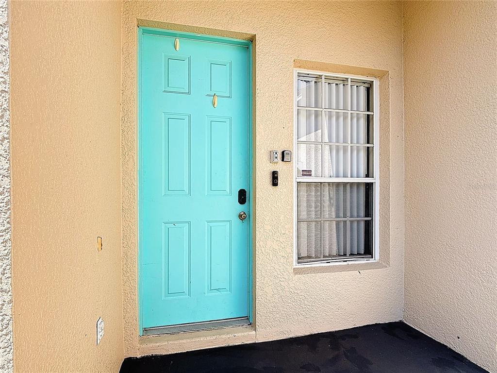 A bright teal front door sits next to a window on a beige stucco porch — 635 KNOLLWOOD DRIVE, DAVENPORT, FL
