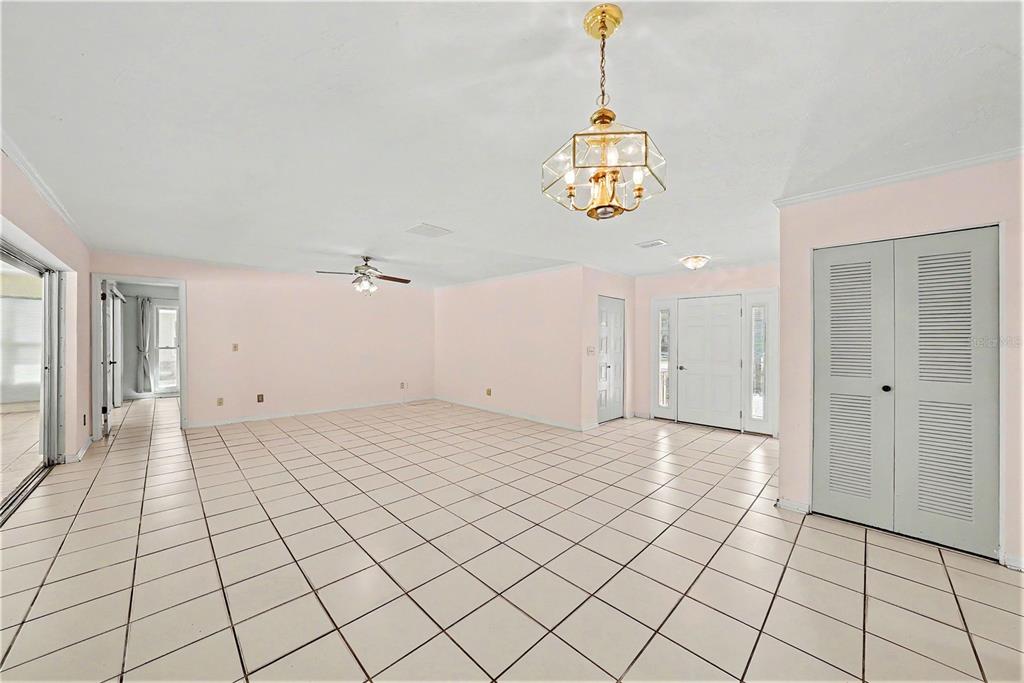 A large, empty room with light pink walls, white tile flooring, and a gold chandelier — 1703 NEW BEDFORD DRIVE, SUN CITY CENTER, FL