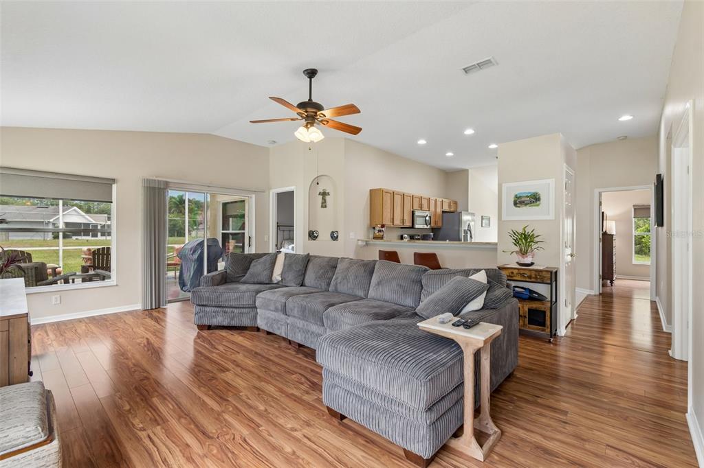 A living room with a gray sectional sofa, wood flooring, and an open kitchen — 20942 SUNSWEET COURT, LAND O LAKES, FL