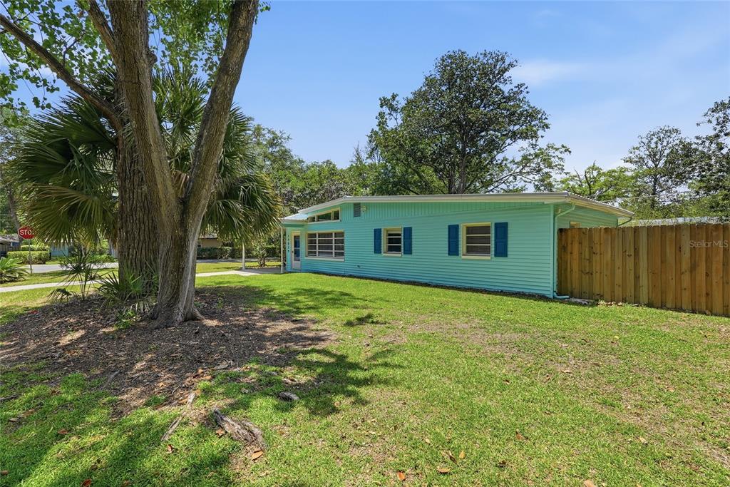 A light blue single-story house with a wooden fence stands on a grassy lawn — 1702 NW 38TH DRIVE, GAINESVILLE, FL