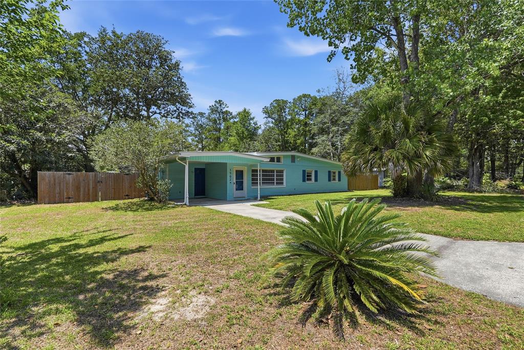 A light blue single-story house with a covered entryway sits on a grassy lot — 1702 NW 38TH DRIVE, GAINESVILLE, FL