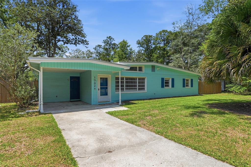 A single-story house with light blue siding, a carport, and a concrete driveway — 1702 NW 38TH DRIVE, GAINESVILLE, FL
