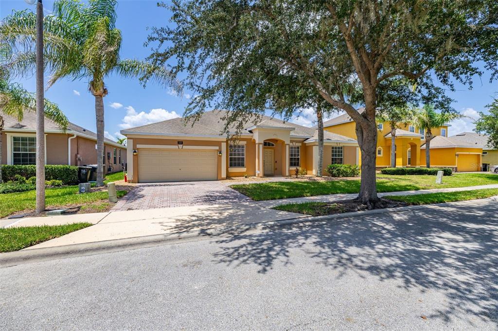 A single-story tan house with a two-car garage and a large tree in the front — 349 YELLOW SNAPDRAGON DRIVE, DAVENPORT, FL