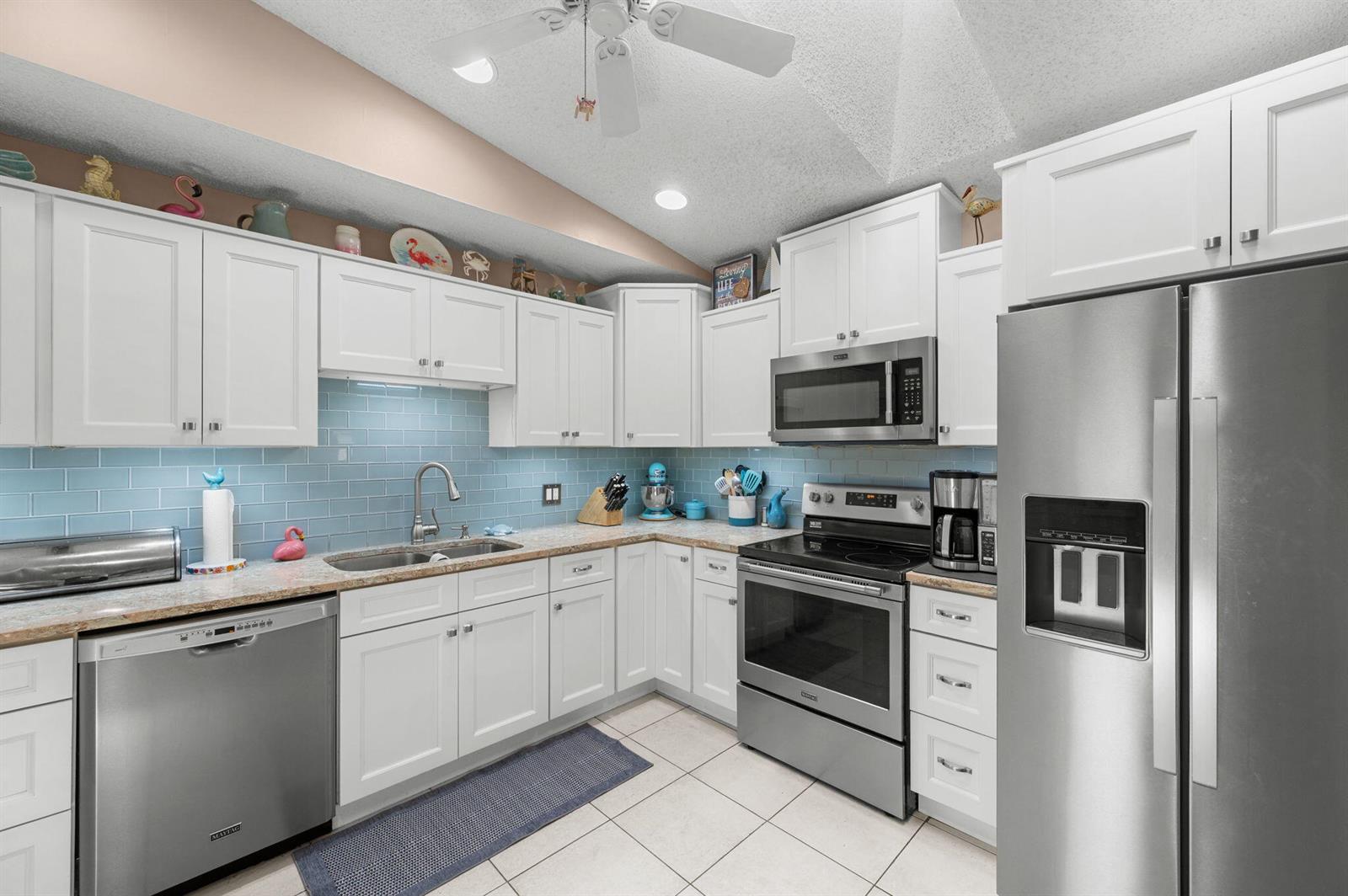 A kitchen features white cabinets, stainless steel appliances, a light blue subway tile backsplash, and tile flooring — 1531 Pheasant Walk # C, Fort Pierce FL 34950, FORT PIERCE, FL