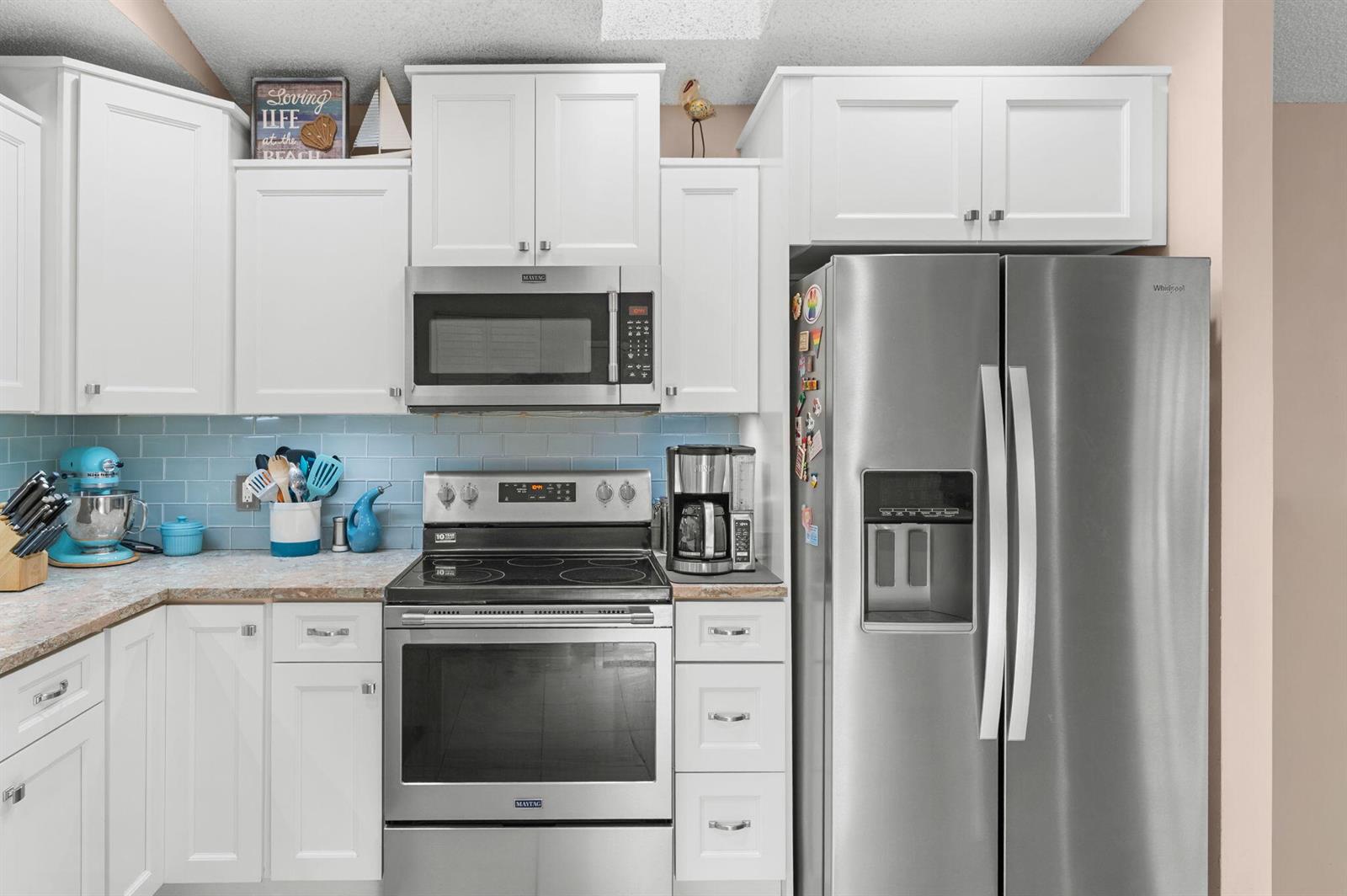 A kitchen features white cabinets, stainless steel appliances, and a light blue tiled backsplash — 1531 Pheasant Walk # C, Fort Pierce FL 34950, FORT PIERCE, FL