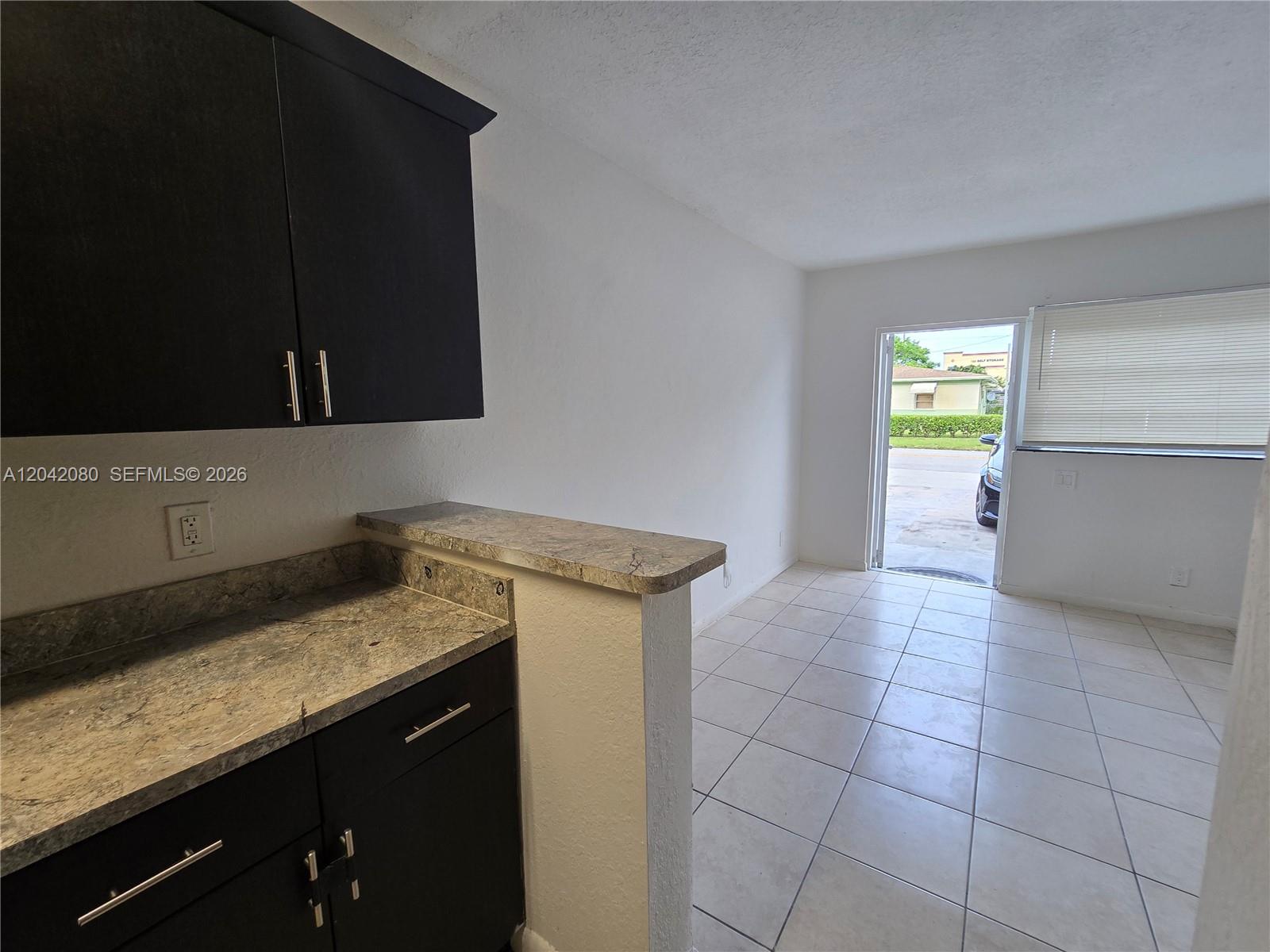 A kitchen with dark cabinets and stone countertops opens into a tiled living area — 2203 Taft St # B, Hollywood FL 33020, HOLLYWOOD, FL