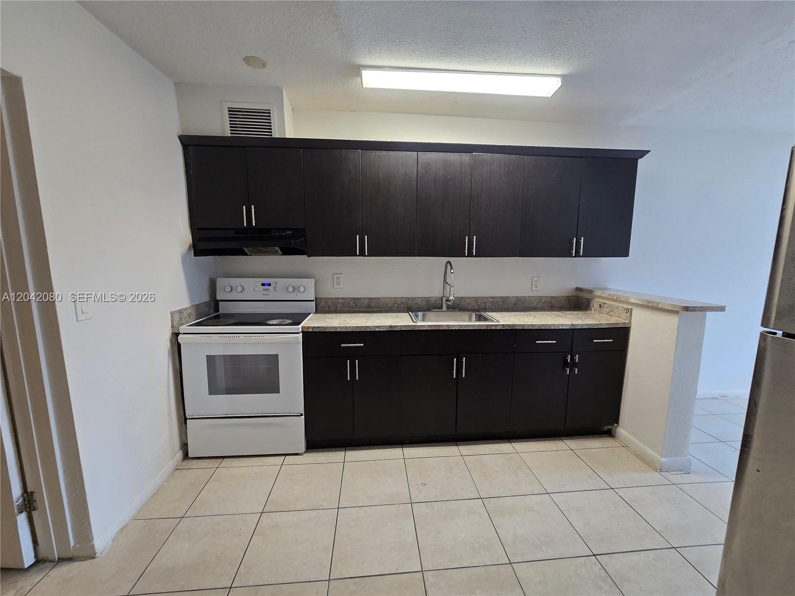 A kitchen features dark wood cabinets, white appliances, a stainless steel sink, and tile flooring — 2203 Taft St # B, Hollywood FL 33020, HOLLYWOOD, FL
