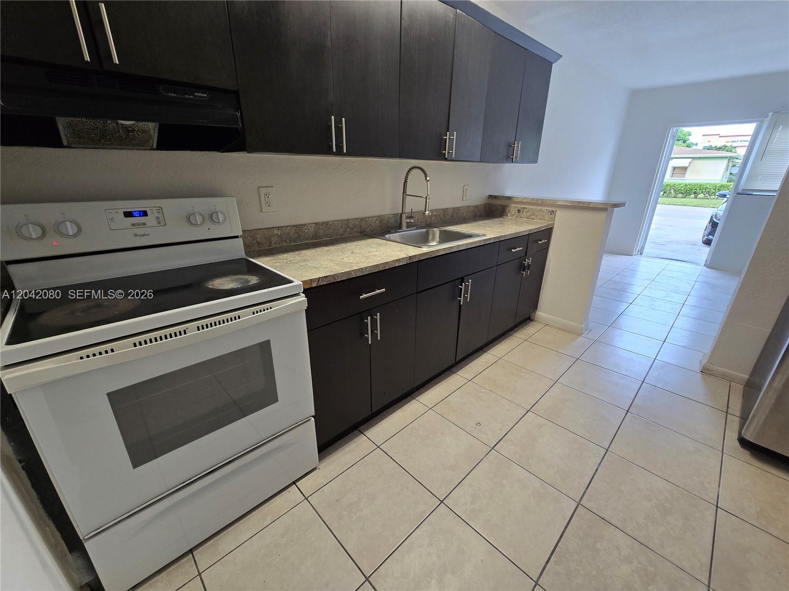 A kitchen features dark wood cabinets, a white stove, and light-colored tile flooring — 2203 Taft St # B, Hollywood FL 33020, HOLLYWOOD, FL