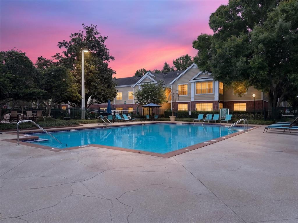A swimming pool sits in front of a two-story apartment building at sunset — 13003 PLANTATION PARK CIRCLE UNIT 1311, ORLANDO, FL