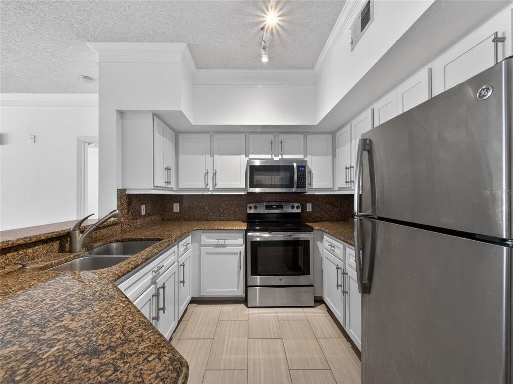 A kitchen features white cabinets, granite countertops, stainless steel appliances, and light-colored tile flooring — 13003 PLANTATION PARK CIRCLE UNIT 1311, ORLANDO, FL