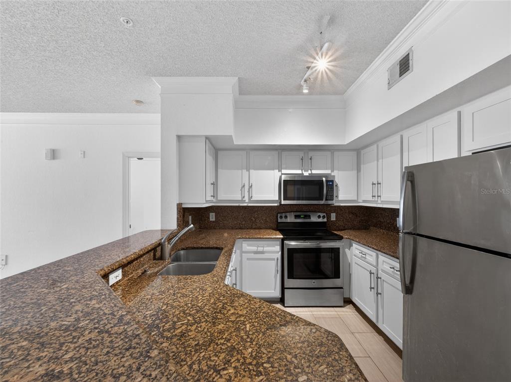 A kitchen features white cabinets, granite countertops, stainless steel appliances, and a breakfast bar — 13003 PLANTATION PARK CIRCLE UNIT 1311, ORLANDO, FL