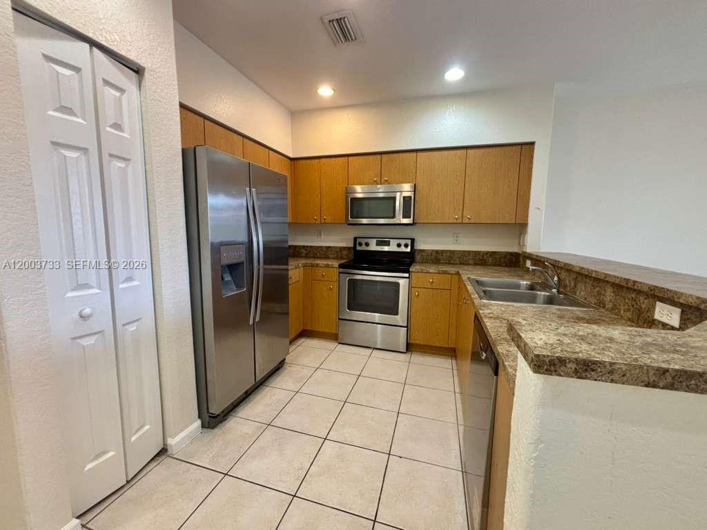 A kitchen features wood cabinets, stainless steel appliances, and a tiled floor — 8375 SW 29th St # 102, Miramar FL 33025, MIRAMAR, FL