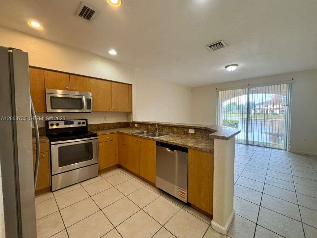 A kitchen with oak cabinets, stainless steel appliances, and tile flooring overlooks a lake view — 8375 SW 29th St # 102, Miramar FL 33025, MIRAMAR, FL