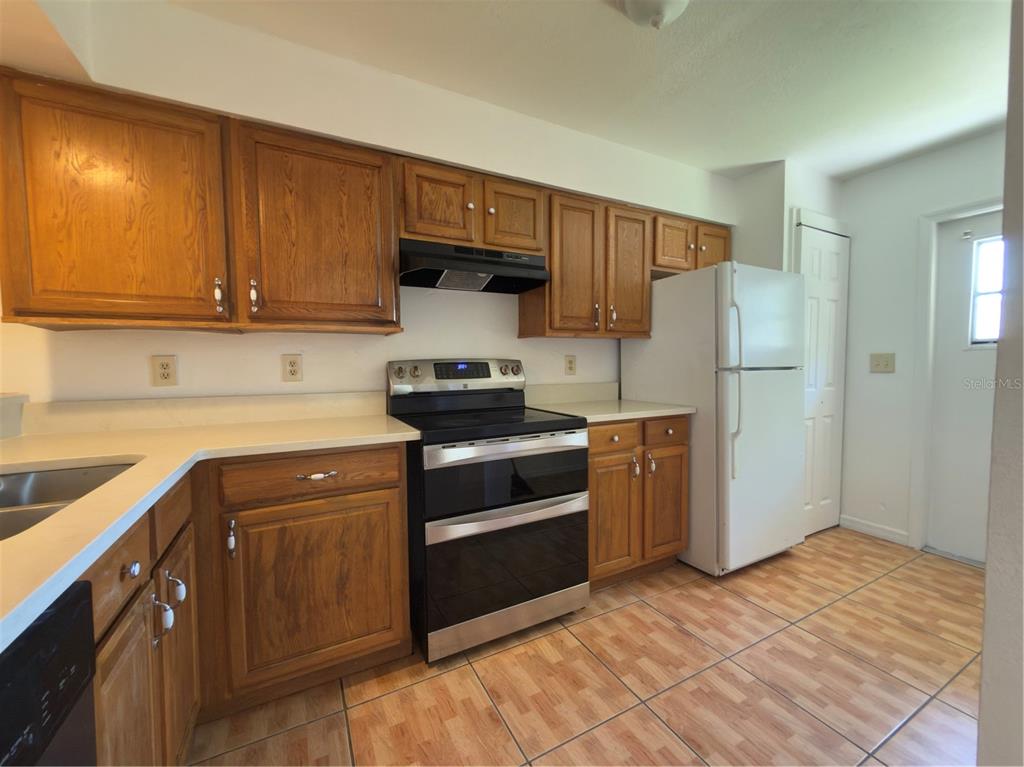 A kitchen features oak cabinets, white countertops, a black stove, and a white refrigerator — 3136 ENCLAVE CT, KISSIMMEE, FL