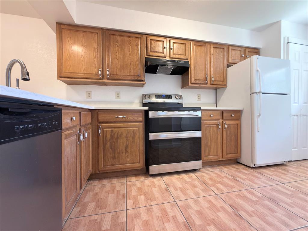 A kitchen features oak cabinets, white countertops, a black dishwasher, and a stainless steel stove — 3136 ENCLAVE CT, KISSIMMEE, FL